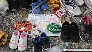 a collection of children's shoes on pavement with rocks and a note in the middle