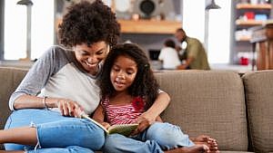 a black mom and daughter sit on the couch reading