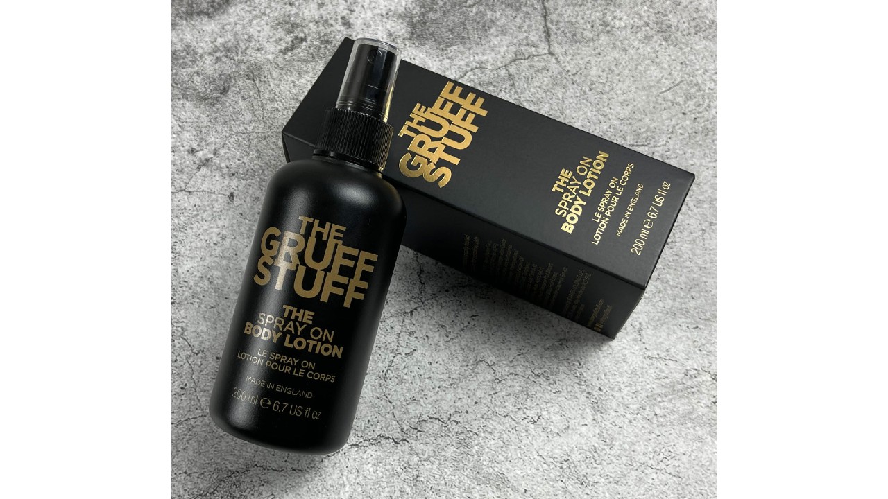 Black body lotion bottle with printed text in gold sitting on top of its similarly designed box