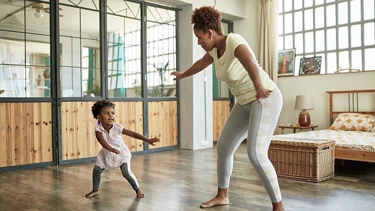 a black woman in leggings dances with her young child indoors