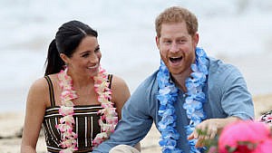 Prince Harry and Meghan Markle laughing on the beach wearing floral garlands