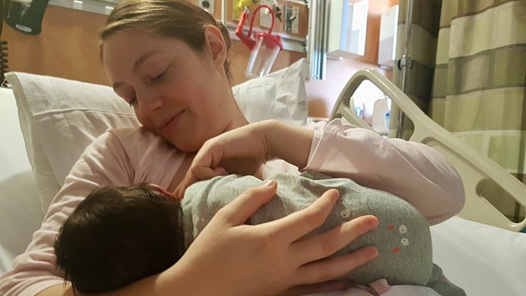 a mom breastfeeding her newborn baby in a hospital bed
