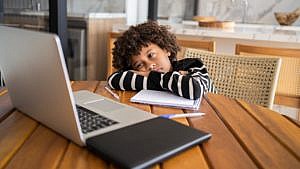 black child sitting at a desk in front of a computer with head down
