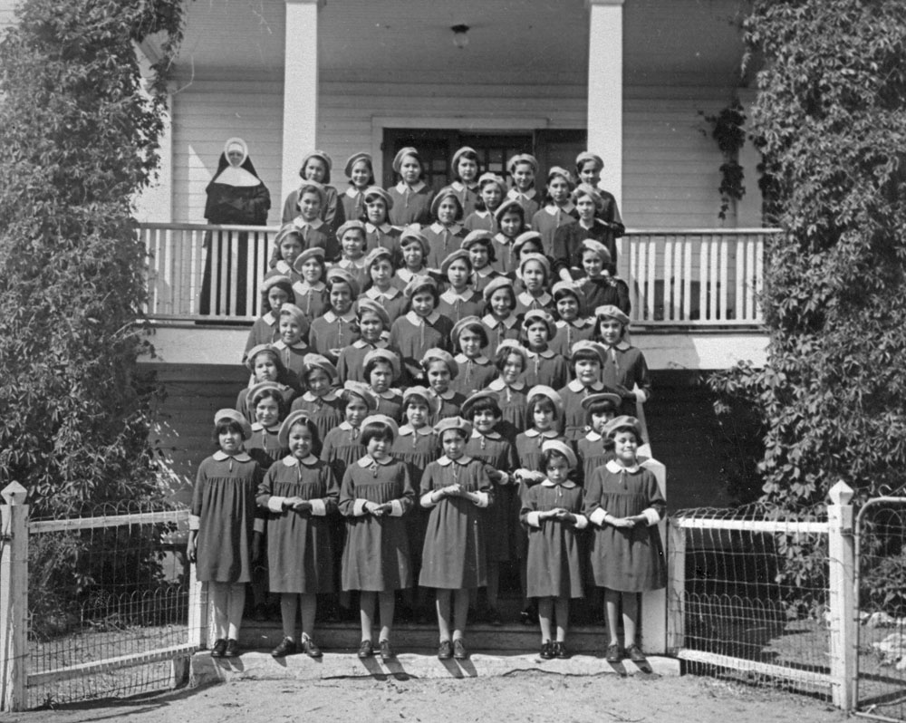 a group of female students and a nun standing outside of a residential school