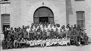 Indigenous children outside of a residential school with staff