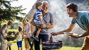 a granddad holds his grandchild outside at a family barbecue