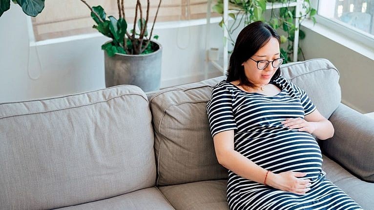 A woman sitting on the couch holding her baby bump