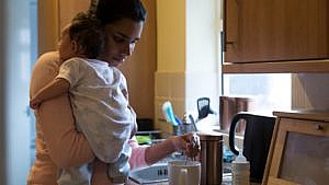 a mom holds her newborn while stirring a cup of coffee in the kitchen