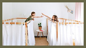 Two girls touch hands from their curtained single beds