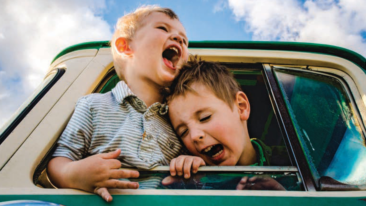 Photo of two kids leaning out of the window of a parked car