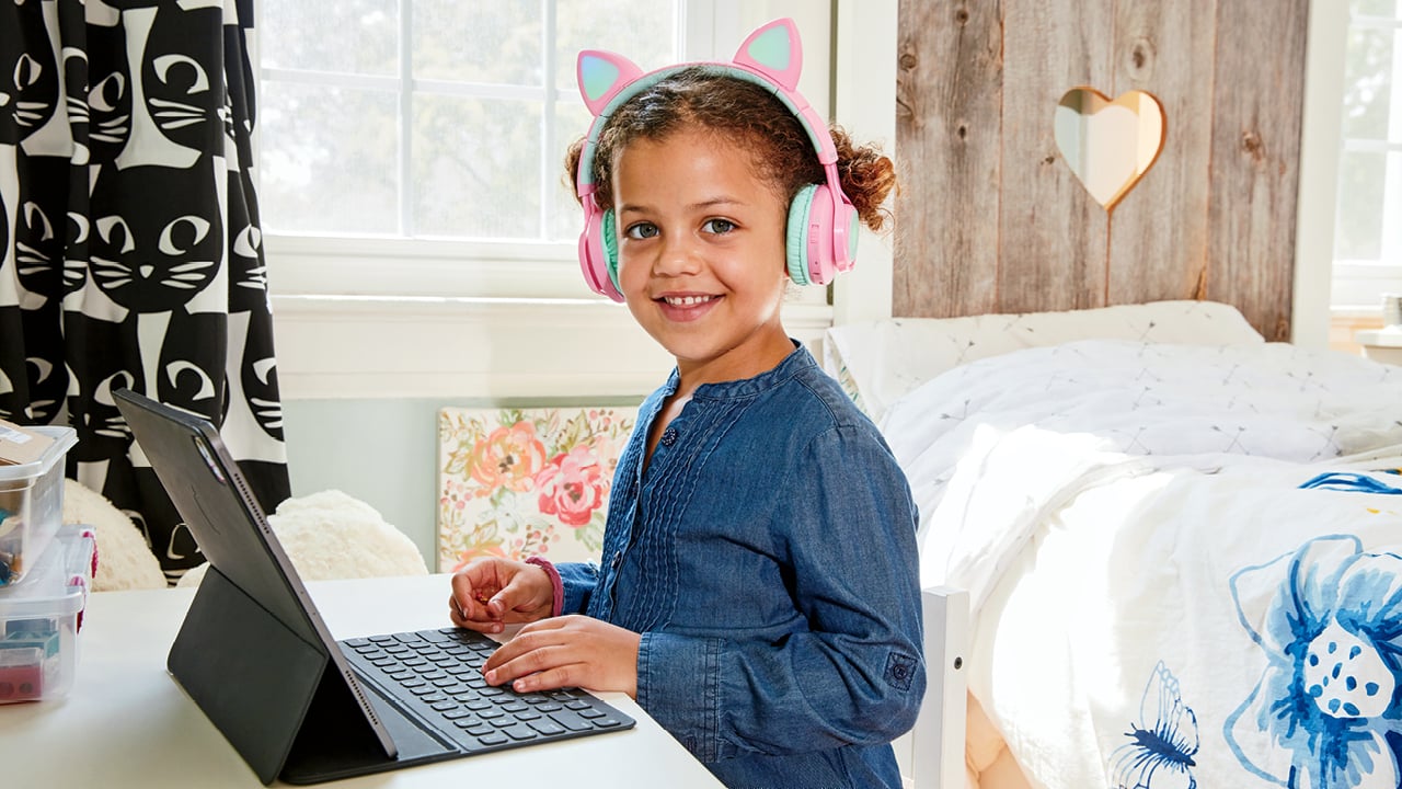 A kid wears animal ear headphones while working on her laptop