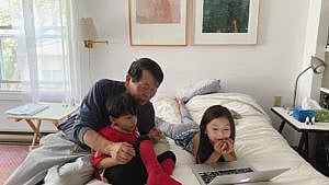 two kids with their grandfather looking at a laptop on a bed