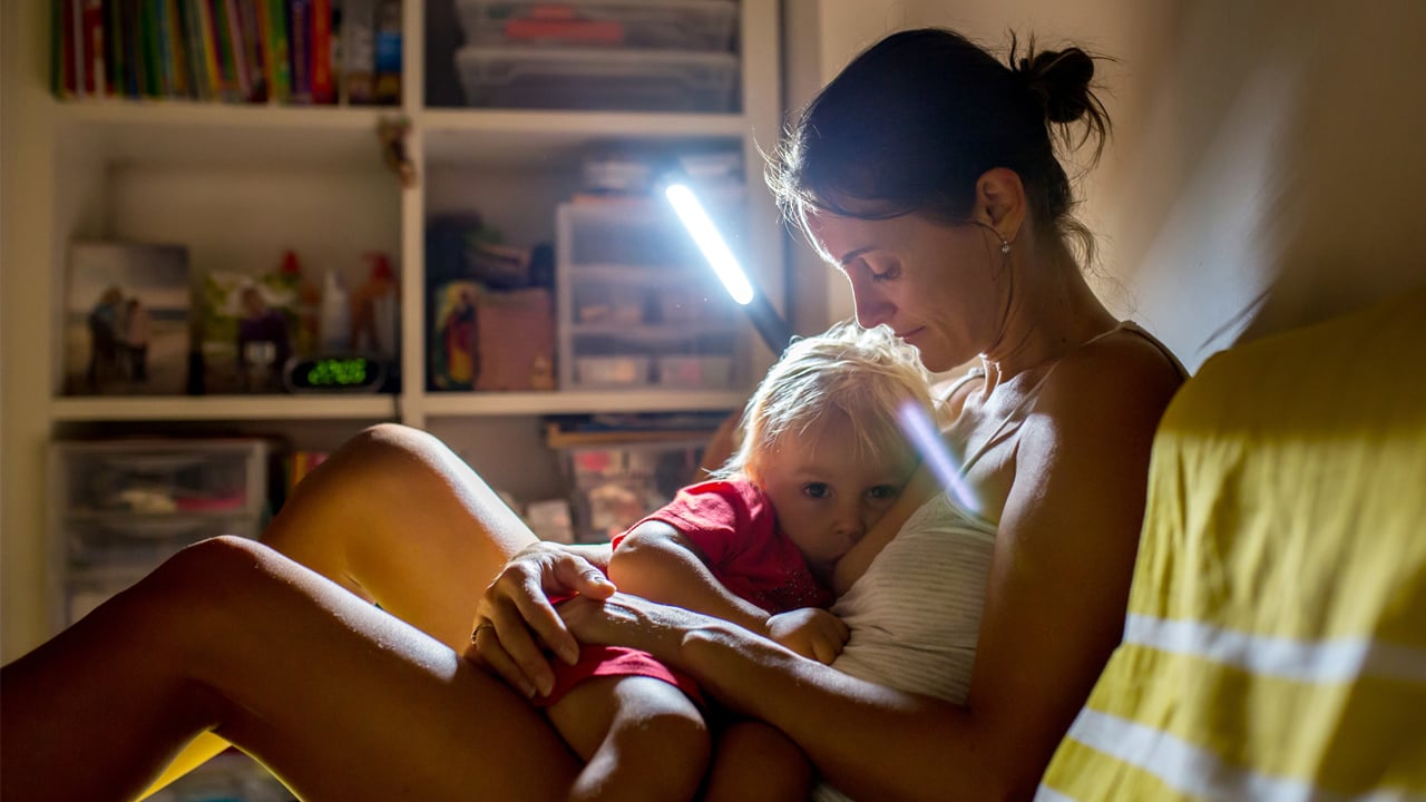 a mother nursing her toddler at night with a lamp on