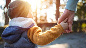 Photo of a kid dressed in fall clothes holding an adults hand while walking outside