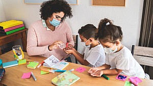 a masked teacher squeezes sanitizer in the hands of two masked children at daycare for a story on the child care platforms of each party in the 2021 Canadian federal election