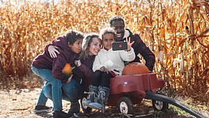 Photo of a family taking a selfie at a corn field with pumpkins in their wagon