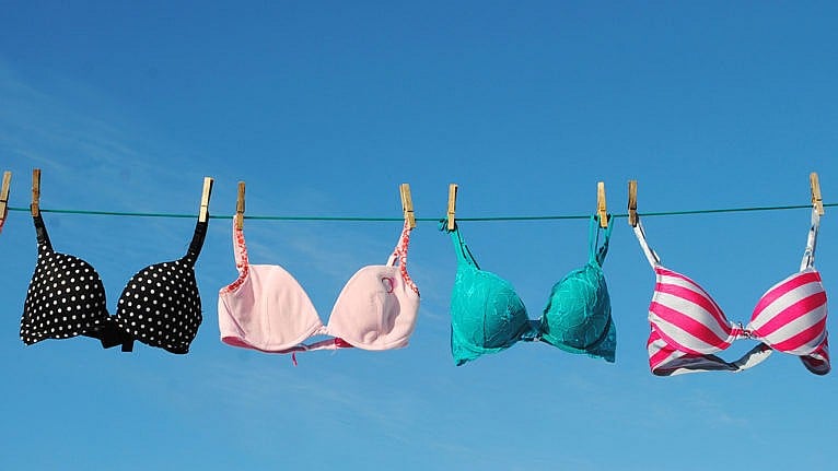 Photo of four colourful bras hanging on a clothesline in the sun against a bright blue sky