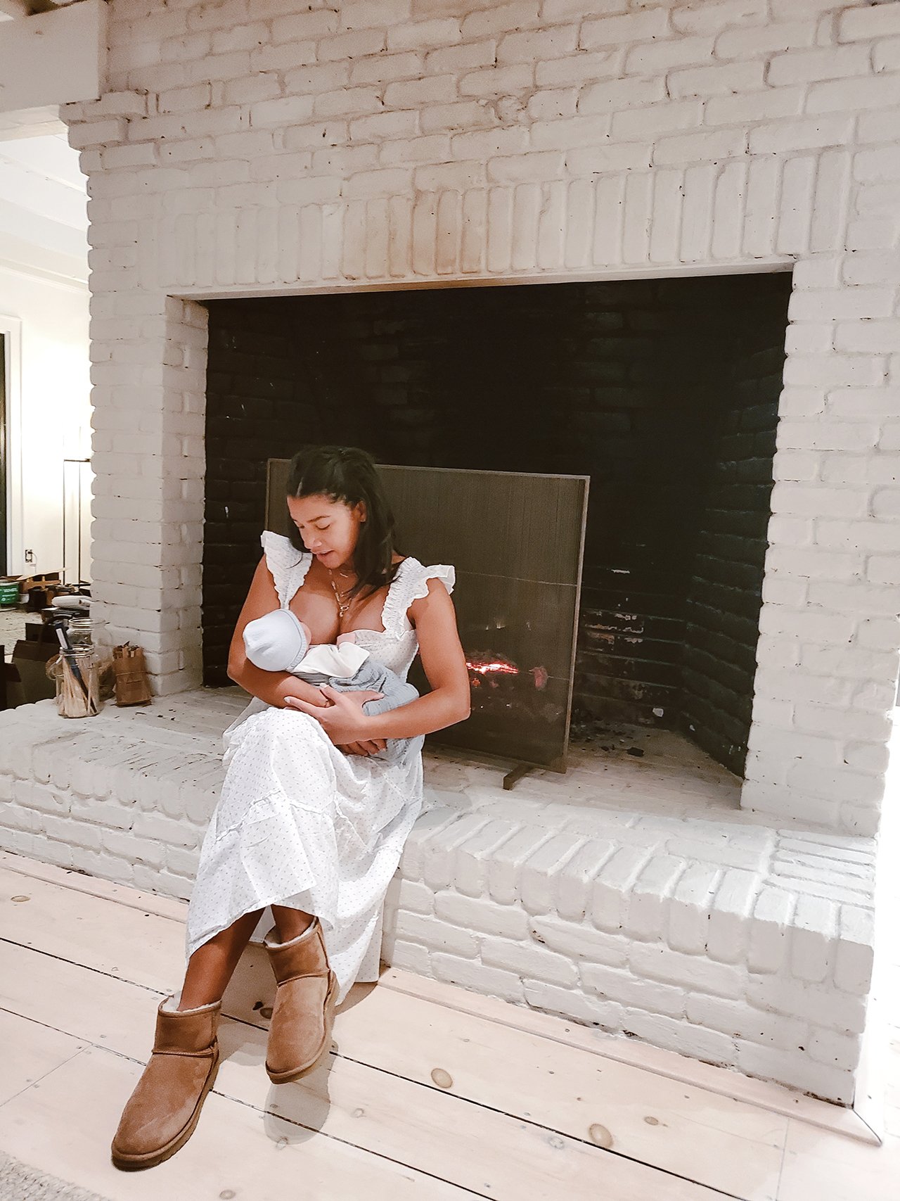 A woman sits at her fireplace breastfeeding her baby from the life after birth coffee table book about the postpartum experience
