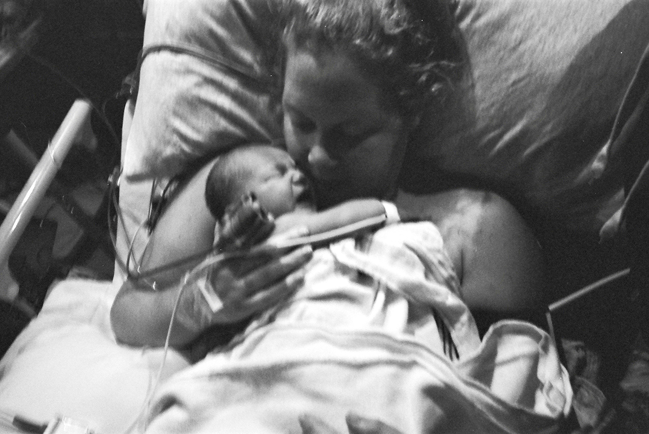 A woman lies in a hospital bed and holds her newborn baby to her chest