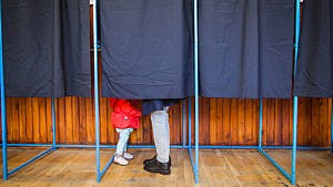 a parent and young child behind the curtain in a voting booth