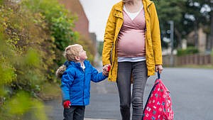 Pregnant parent walking their kid to school holding hands