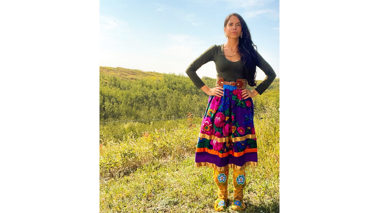 A woman is standing in a meadow and wearing a brightly colored skirt