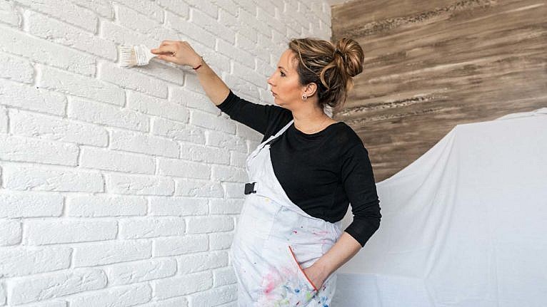 Photo of a pregnant woman painting brick wall in white