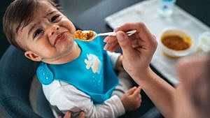 A photo of a baby refusing to eat food from a spoon.