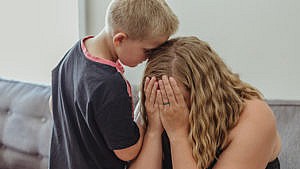 a woman holds her face in her hands while her son stands next to her