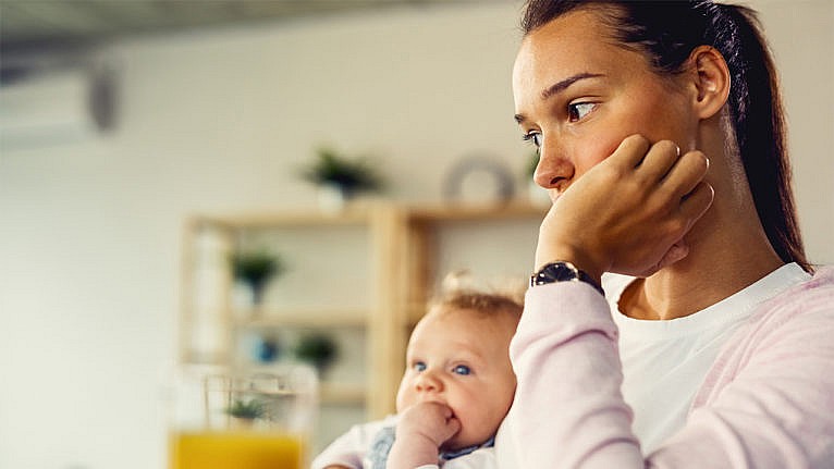 A woman sits with her chin in her hand while holding her baby