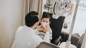 An eye doctor holds a child's face while examining his eyes