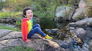 A young boy smiling for the camera sitting beside a waterfall