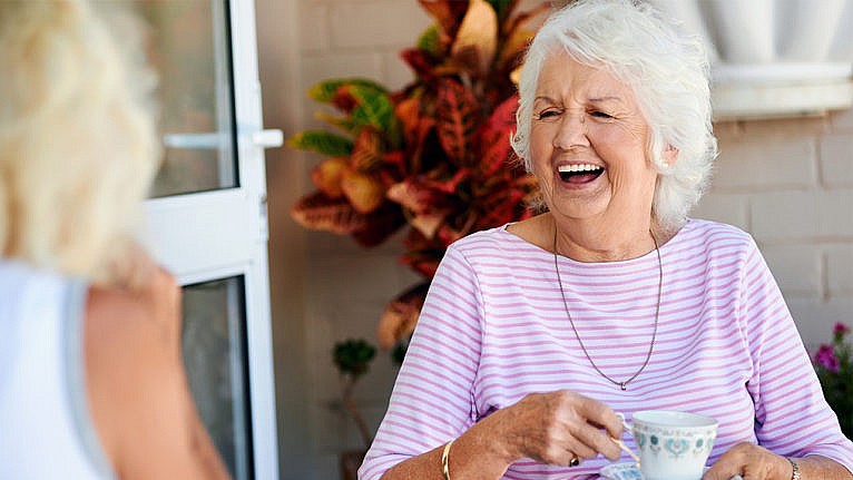 photo of an older woman laughing while drinking tea with some friends