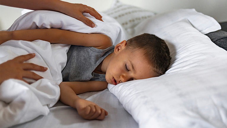Photo of a little kid lying in bed while a parent checks on them