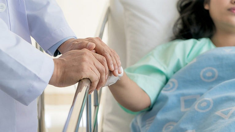 a doctor holding a woman's hand who is lying in a hospital bed