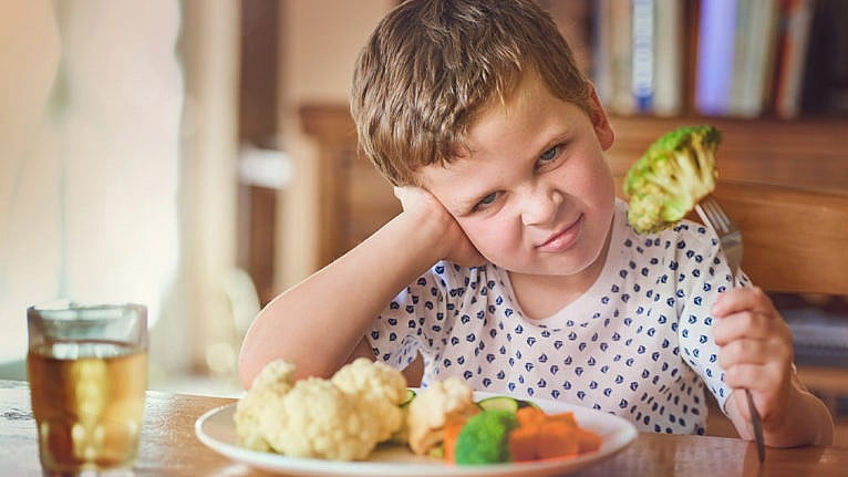 Photo of a kid holding a fork with a piece of broccoli on it. The kid has a look of disgust on their face