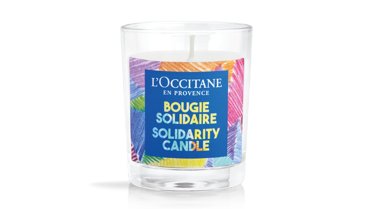 White candle in clear jar with colourful label that reads "Solidarity Candle"