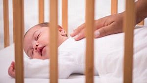 a baby sleeps in the crib with a parent's hand on their chest