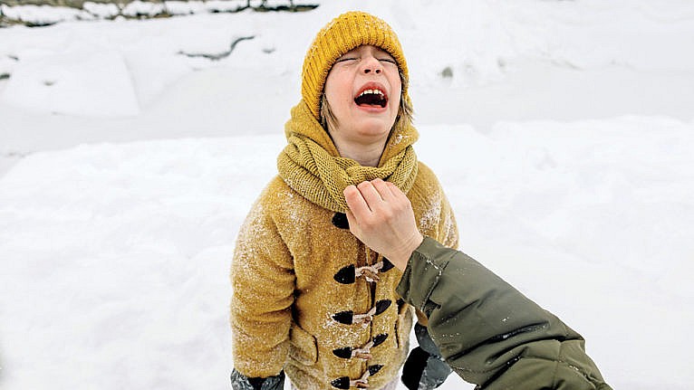 child wearing a yellow jacket and a yellow toque cries as a hand holds his coat