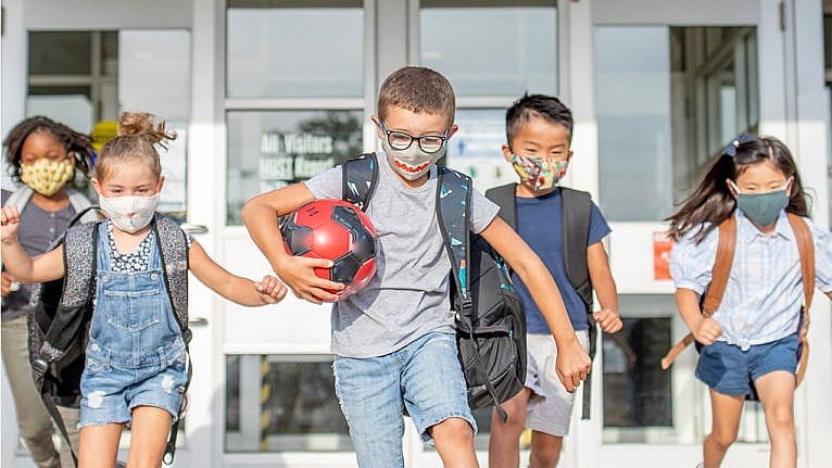 Children wearing masks exit their school together