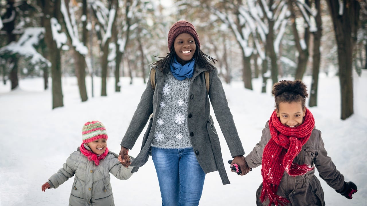 A mom and two children walk along a snowy trail.