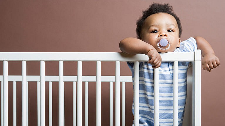 a photo of a baby with a paci standing in their crib