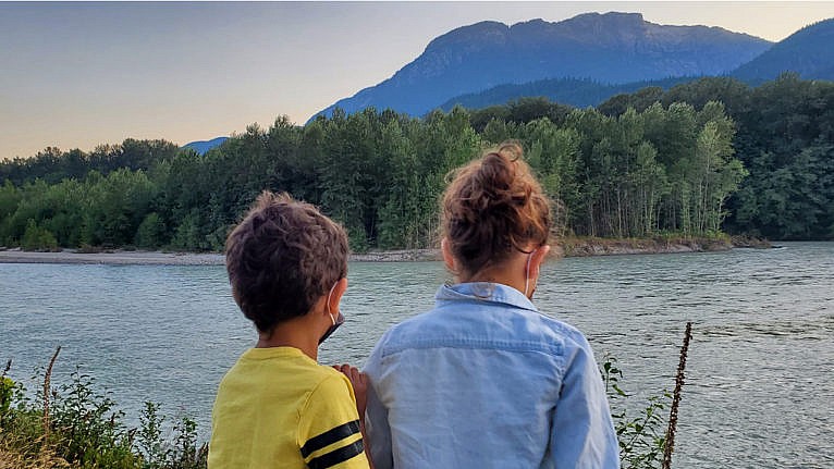 two kids from behind standing side by side looking out at a lake and mountains in the distance