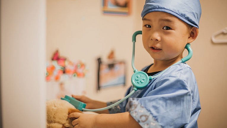 a little boy in scrubs and a stethoscope playing doctor with his stuffie