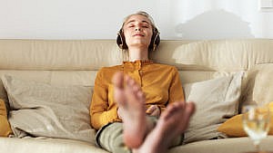 Photo of a person sitting on the couch with their feet up on the coffee table listening to something on their headphones
