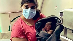Aisha Khatib, a travel doctor and professor, holds the healthy baby girl who she just delivered while on a flight. The baby is swaddled in a grey blanket as Khatib poses with her inside the plane.
