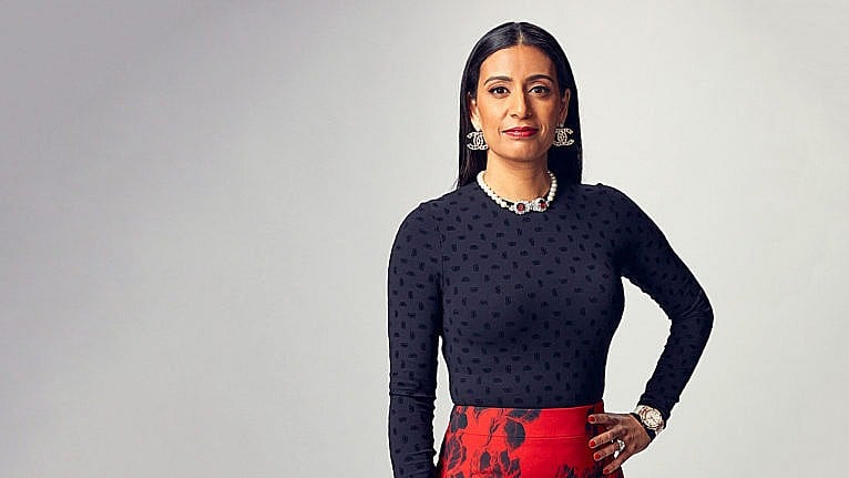 A photo of Dragon's Den star Manjit Minhas posing in a black long sleeve and red skirt with her hand on her hip