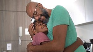 A father with a beard and glasses hugging his son wearing glasses.