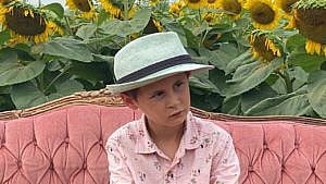 A boy sits on a couch in front of a sunflower field.