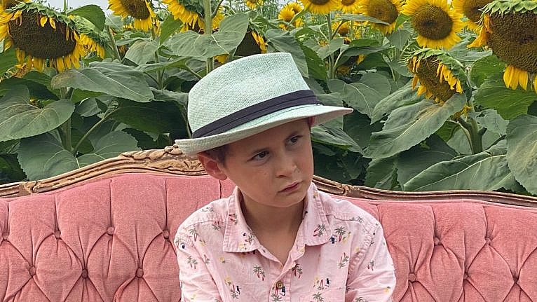 A boy sits on a couch in front of a sunflower field.